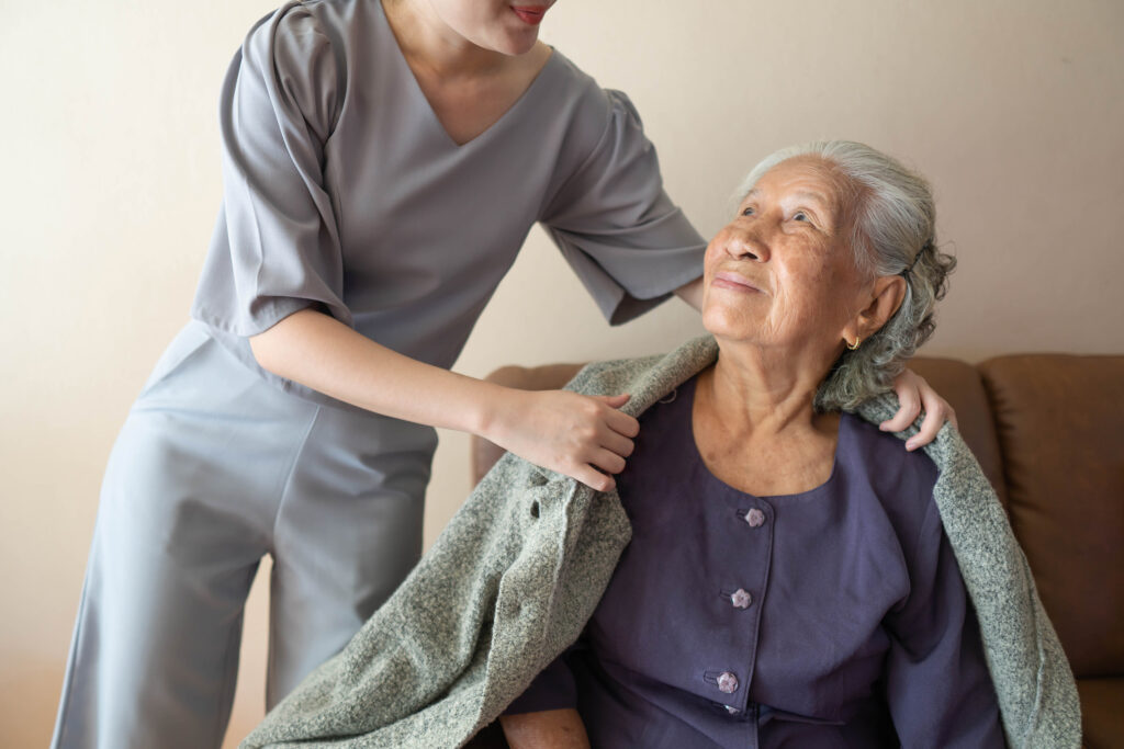 Elderly woman having sweater draped over her shoulders by another person