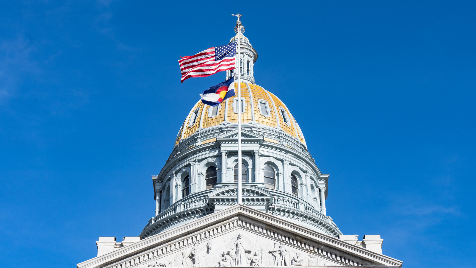 Photograph of the Colorado State Capitol building in Denver, showcasing its iconic gold-domed roof and neoclassical architecture. The structure features a grand staircase leading to the entrance, with the dome gleaming under the sunlight, symbolizing Colorado's rich history and governance.
