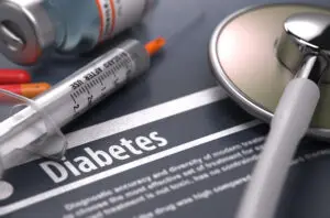 A close-up of a medical scene with a syringe, vials, and a stethoscope resting on a document labeled "Diabetes." The focus is on the syringe and the word "Diabetes," suggesting a context related to diabetes management or prescription medications.
